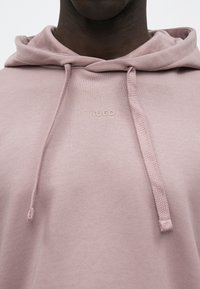 Svetloružová mikina s kapucňou z bavlnenej zmesi, vybavená šnúrkou na kapucni a malým vyrazeným logom na hrudi. Hladká textúra, ležérny dizajn.