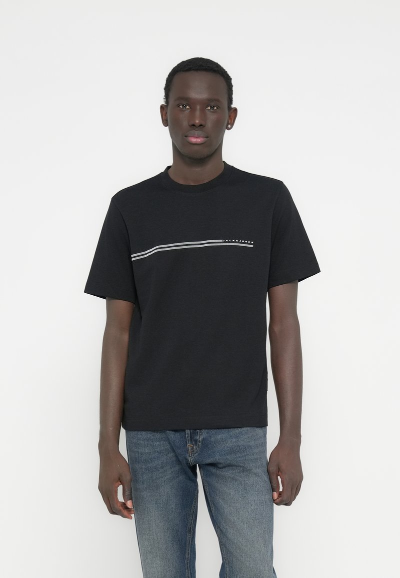 Μαύρο βαμβακερό μπλουζάκι με λευκή οριζόντια γραμμή στο ύψος του στήθους, συνδυασμένο με μπλε τζιν. Απλός σχεδιασμός με λαιμόκοψη τύπου crew.