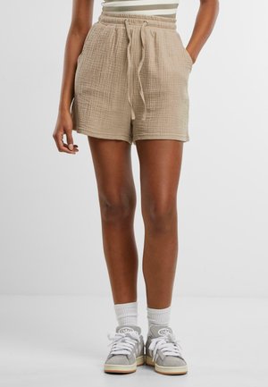 Beige textured shorts with an elastic waistband and drawstring, featuring side pockets. Pairing with gray sneakers and white crew socks.