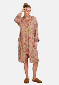 Beige kimono-stijl jas met bloemenpatroon en zakken. Beschikt over lange mouwen met gestreepte manchetten. Gemaakt van lichte stof.