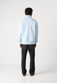 Sudadera azul clara con cuello alto, puños y dobladillo acanalados. Combinada con pantalones holgados negros y zapatos marrones.