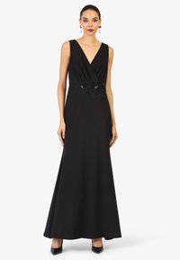 Robe noire sans manches avec un décolleté en V plongeant, un corsage texturé enroulé et une accent en dentelle florale à la taille. Jupe évasée longueur sol.