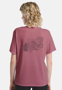 T-shirt rose avec une illustration graphique noire de montagnes, de lignes et de feuilles au dos, à manches courtes et à coupe décontractée.