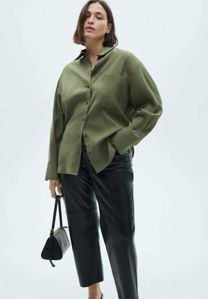 Olijfgroene, oversized button-up shirt met een kraag, gecombineerd met strakke zwarte leren broeken. Geaccentueerd met een kleine zwarte handtas.