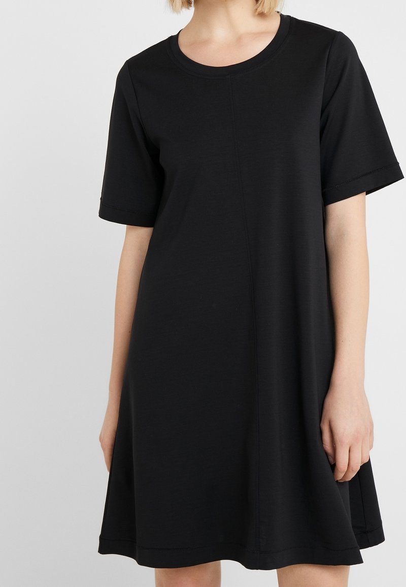 Robe noire à manches courtes en tissu doux, avec un col rond et une silhouette trapèze ornée de coutures apparentes.