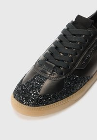 Baskets noires en cuir verni texturé avec un embout pailleté. Dotées d'une semelle en caoutchouc de couleur caramel et de lacets plats noirs.
