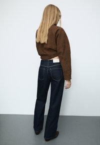 Ruskosuinen mokkajakku, joka on lyhyt ja yhdistetty tummansinisiin korkeavyötäröisiin suoralahkeisiin farkkuihin, joissa on kultainen ommel ja kaksi takataskua.