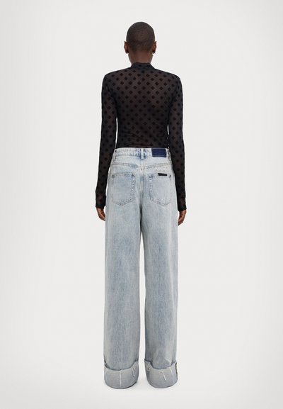 Blusa negra transparente de manga larga con patrón de diamante, combinada con unos vaqueros de pierna ancha azul claro que presentan dobladillo doblado y bolsillos traseros.