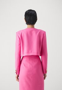 Giacca da abito rosa aderente con spalle strutturate, design cropped e maniche lunghe, con dettagli in bottoni dorati sui polsini.