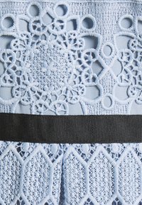 Tissu délicat en dentelle bleu clair avec des motifs circulaires et en losange complexes et un ruban noir texturé au milieu.
