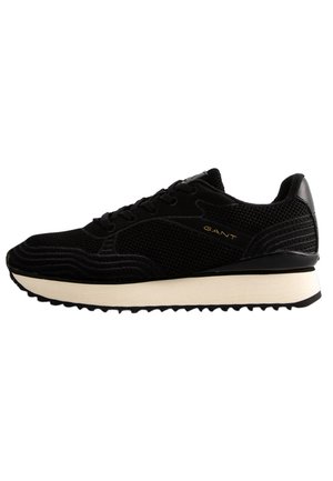 Black athletic shoe with a textured mesh upper, featuring contrasting smooth accents and a white sole with a zigzag tread pattern.