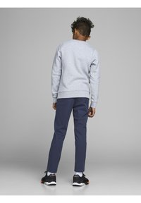 Niño con cabello rizado de espaldas, viste un sudadera gris claro, pantalones azul marino, calcetines blancos y zapatillas negras con acentos naranjas.