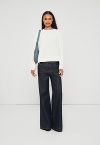 Sweatshirt branca com um corte corto, combinado com jeans de perna larga azul escuro. Uma mala azul de ombro complementa o look. Design simples.
