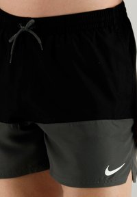 Costumi da bagno neri e grigi realizzati in tessuto leggero, con una cintura elastica dotata di coulisse e un logo bianco sulla parte inferiore.