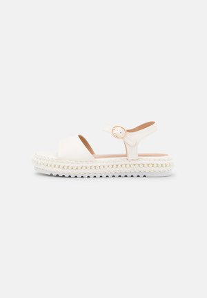 Sandale blanche à bout ouvert avec bride à la cheville, boucle dorée et semelle plateforme épaisse avec des détails tressés et perles.