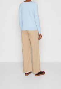 Maglione azzurro chiaro a maniche lunghe, pantaloni beige a gamba larga e sneakers scuri con dettagli bordeaux. Texture liscia, vestibilità casual.