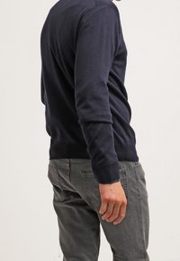 Granatowy sweter dzianinowy z ściągaczami u rękawów i na dolnej krawędzi, uzupełniony o szare teksturowane spodnie. Sweter ma okrągły dekolt i taliowany krój.