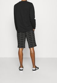 Czarna koszula z długim rękawem w połączeniu z czarnymi szortami z powtarzającym się białym logo "CALVIN KLEIN". Uzupełnione czarno-białymi trampkami marki Nike.