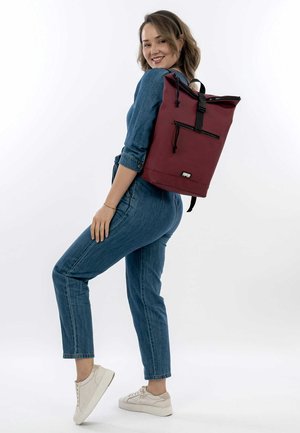 Mochila burdeos con diseño de rollo, correas de hombro ajustables y un bolsillo frontal con cremallera; hecha de tela duradera, textura suave.