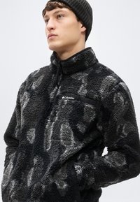 Μαύρο και γκρι fleece πουλόβερ με ψηλό γιακά, φερμουάρ στο μπροστινό μέρος και πλαϊνές τσέπες, με υφή απαλή στην επιφάνεια και λογότυπο στο στήθος.