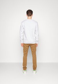 Sweat-shirt gris clair avec poignets côtelés, accompagné d'un pantalon marron. La tenue est complétée par des baskets blanches avec des accents verts.