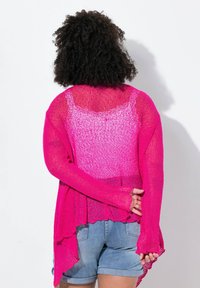 Ljust rosa, lättstickad cardigan med en svepande design, öppen fram, långa ärmar och en vågig nederkant, lager på en ljusare topp.