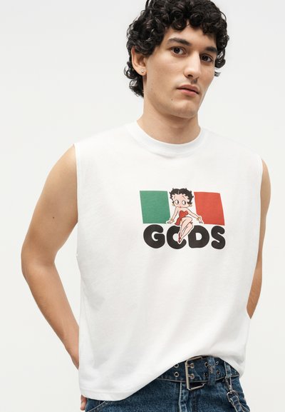 Νέος με σγουρά μαλλιά που φοράει αμάνικο λευκό μπλουζάκι με χαρακτήρα κινουμένων σχεδίων και τα χρώματα της ιταλικής σημαίας στο μπροστινό μέρος.