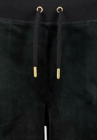 Melni treniņbikses ar mīkstu tekstūru, kurām ir melna josta, melns aukla ar zeltainiem metāla galiem un caurumiem.