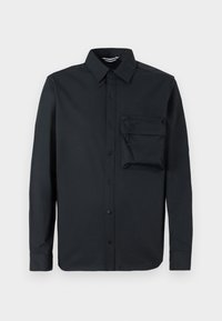 Camisa negra de manga larga hecha de una tela suave. Presenta un cuello abotonado y un bolsillo en el pecho izquierdo con cierre de cremallera. Ajuste clásico.