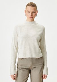 Sweter w kolorze kremowym, prążkowany, z wysokim kołnierzem, długimi rękawami i skróconą konstrukcją. W zestawie ze światem beżowymi dopasowanymi spodniami.