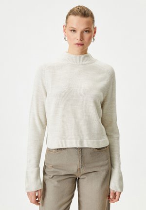 Krämfärgad, ribbad stickad tröja med hög krage, långa ärmar och en kort design. Matchad med ljusbeige, åtsittande byxor.