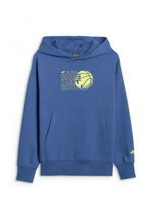 Dziecko z kręconymi włosami, ubrane w niebieską bluzę z kapturem do koszykówki, pasujące spodnie dresowe i granatowe sneakersy, stoi z rękami w kieszeniach.