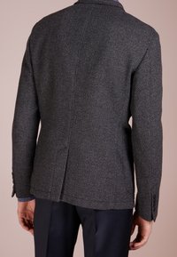 Blazer grigio intrecciato con un sottile motivo a spina di pesce, rever a scapola, spacco singolo e polsini abbottonati, abbinato a pantaloni scuri.