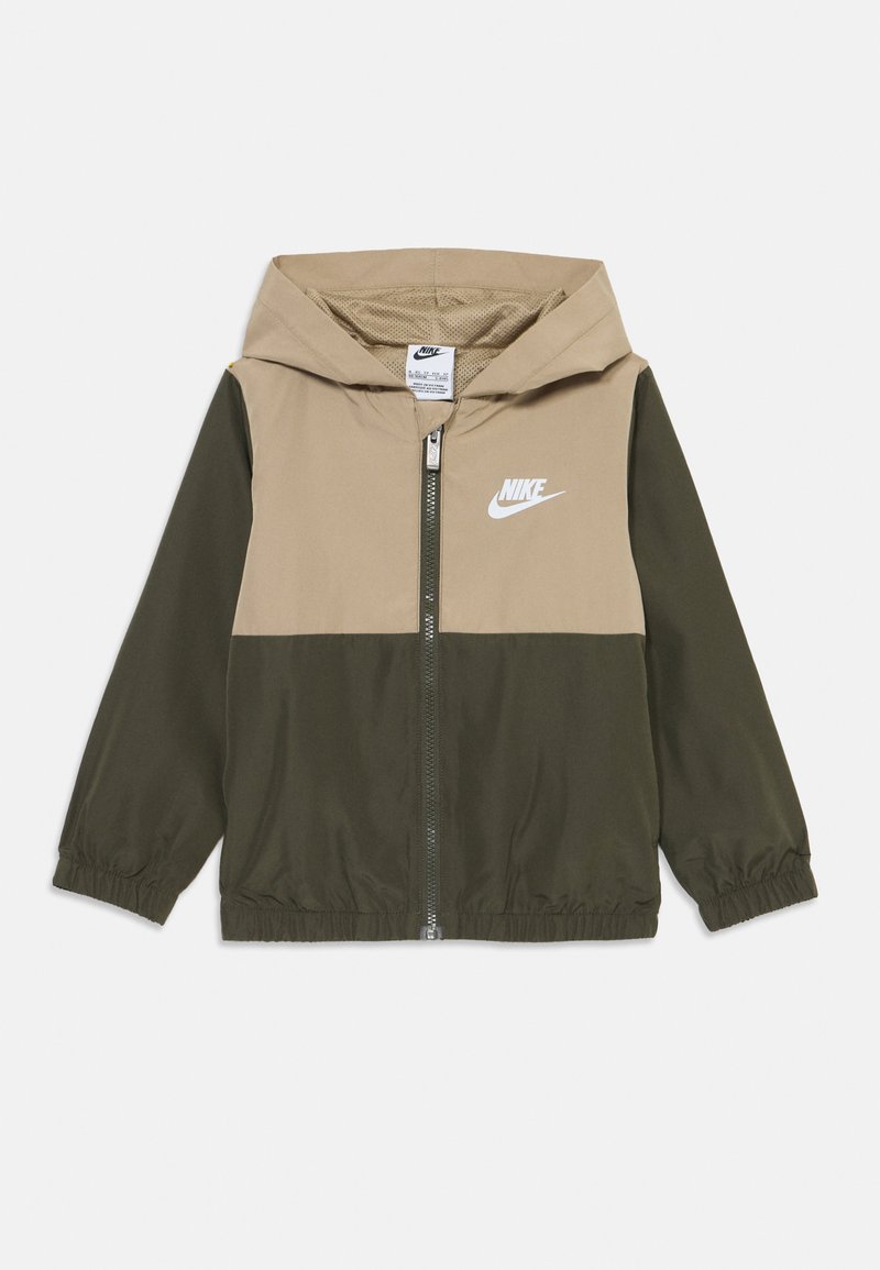 Nike Windbreaker-Jacke mit einem beigen oberen Teil und dunkelkarierten unteren Paneelen. Sie verfügt über eine Kapuze, einen Reißverschluss und elastische Bündchen. Logo auf der Brust.