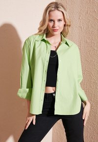 Camicia verde chiaro in cotone, con vestibilità comoda, colletto a punta e maniche lunghe arrotolate ai polsi.