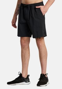 Black shorts made of lightweight fabric, featuring an elastic waistband and side pockets. Worn with black athletic sneakers.