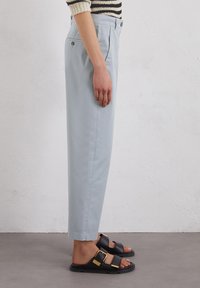 Chinos bleu clair avec une coupe droite, dotés de poches latérales et d'une texture élégante, associés à des sandales noires avec des accents en boucle dorée.
