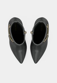 Botines negros de punta afilada con detalles de hebilla dorada en los laterales, vistos desde arriba sobre un fondo blanco.