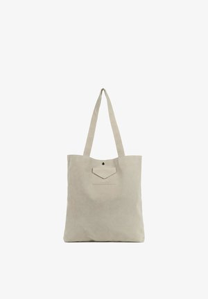 Sac fourre-tout en toile beige avec deux longs anses, une poche avant avec rabat, et un design minimaliste. Texture lisse et lignes simples et épurées.