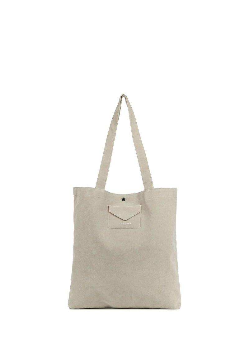 Sac fourre-tout en toile beige avec deux longs anses, une poche avant avec rabat, et un design minimaliste. Texture lisse et lignes simples et épurées.