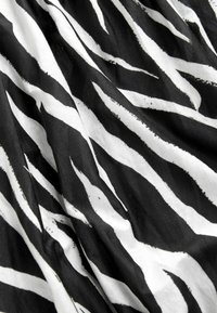 Crno-bijela tkanina s uzorkom zebra pruga. Tekstura izgleda glatko s hrabrim, naizmjeničnim zupčastim linijama različitih širina.