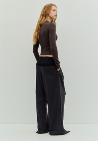 Langärmliges braunes Oberteil kombiniert mit locker sitzender, dunkelgrauer Hose mit Nadelstreifen, ausgestattet mit einem elastischen Bund und Seitentaschen.