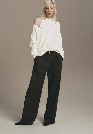 Suéter de crema de gran tamaño con detalles recortados combinado con pantalones de pierna ancha negros de tiro alto. Textura suave; diseño minimalista.