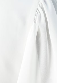 Vit blus i mjukt, lättviktigt tyg med mjuka draperingar. Har en rynkad detalj på ena sidan för extra textur.