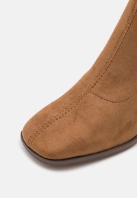 Brun mockaskinn stövlet med hög klack och spetsig tå, med subtila sömmar och en jämn yta på ovandelen, kombinerad med en hållbar sula.