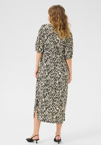 Mid-length dress in lightweight fabric with a black and cream abstract pattern. Features puff sleeves and a side slit.