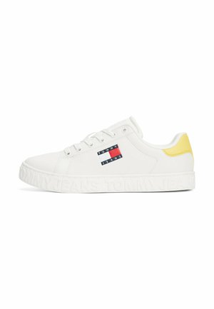 Baskets blanches en matériau synthétique texturé. Elles présentent un accent jaune au niveau du talon, ainsi qu'un patch logo avec un design bleu, rouge et blanc.