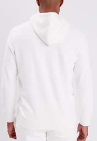 Sudadera blanca con capucha, tejido suave, corte relajado, puños y dobladillo acanalados, con un bolsillo tipo canguro, sin logotipos ni patrones visibles.