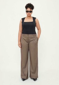 Black sleeveless top paired with high-waisted, wide-leg brown trousers. Model wears dark sunglasses and pointed black shoes.