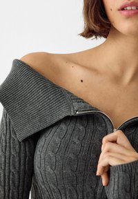 Gray ribbed sweater with a cable knit pattern, off-shoulder design, and silver zipper closure. Soft texture and prominent collar detail.